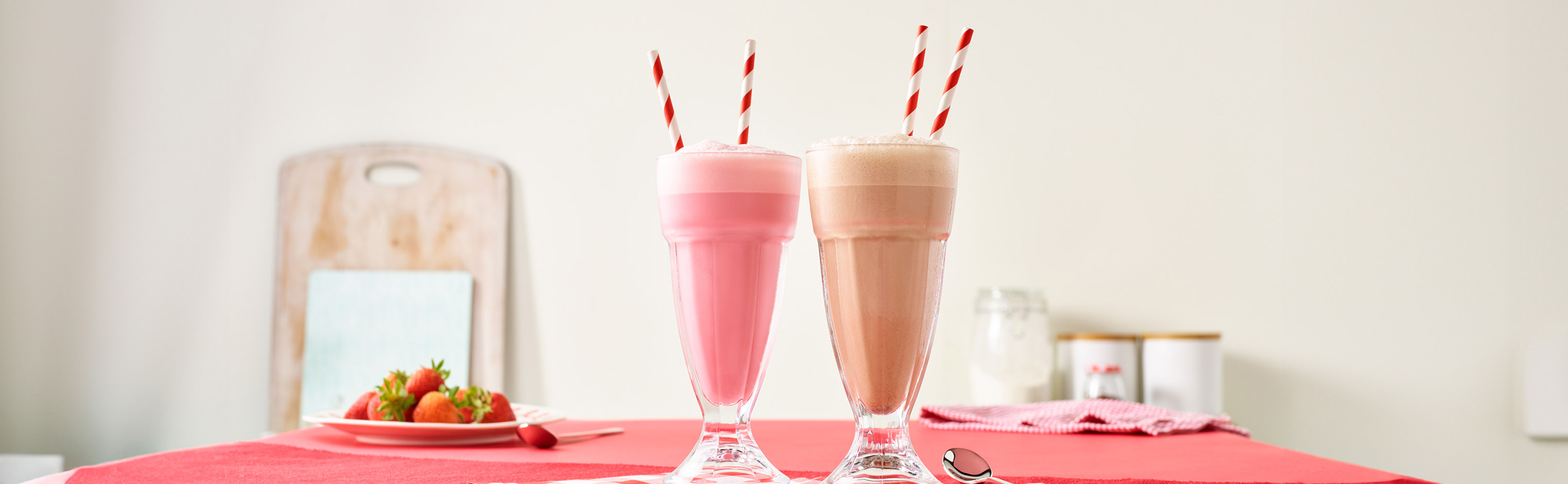 Crusha Milkshake Mix bottles alongside two milkshakes in tall glasses with stripy straws.